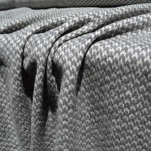 a close-up view of a fabric with a distinctive gray and white checkered pattern. The fabric appears to be made of wool or a similar material, and it is folded or crumpled, creating a textured and visually interesting surface.