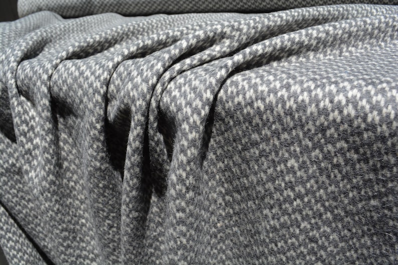 a close-up view of a fabric with a distinctive gray and white checkered pattern. The fabric appears to be made of wool or a similar material, and it is folded or crumpled, creating a textured and visually interesting surface.