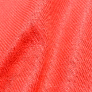 May include: Close-up of a vibrant red fabric with a textured, diagonal weave pattern. The material is soft and appears to be draped, with subtle shadows adding depth. The overall impression is of a warm, inviting textile.