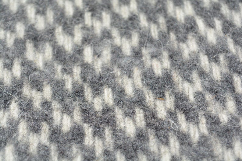 A close-up image of a textured fabric with a pattern of small white and gray squares or rectangles.