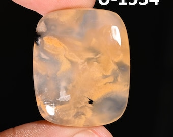 May include: A polished, rectangular gemstone with rounded corners, featuring a translucent, milky base with swirling patterns of soft orange and gold, accented by small, distinct black inclusions and the text U-1534.