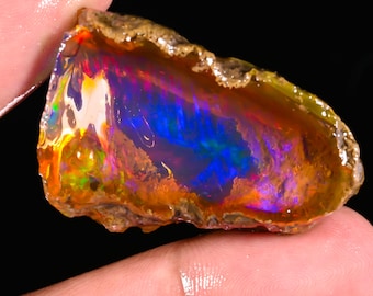 May include: A vibrant, raw opal gemstone with a spectrum of colors including blue, orange, yellow, and purple. The opal has a rough, textured exterior and a polished, iridescent interior, showcasing a play of light.