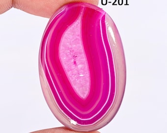 May include: An oval-shaped polished gemstone featuring vibrant concentric bands of hot pink and white, with a textured, crystalline center. The stone is marked with the text U-201 in the upper right corner, showcasing a smooth, glossy surface.