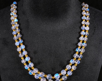 May include: A double-strand necklace featuring alternating round, translucent moonstone beads with a blue iridescent sheen and smaller, metallic gold-toned spherical beads arranged in a repeating pattern along the entire length of the jewelry piece.