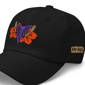 May include: Black baseball cap with embroidered design. The design features a purple geometric shape, orange flowers, and the text "BAY AREA" in a gold color. The cap has a curved brim.