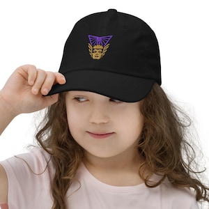 May include: Black baseball cap with a purple and gold embroidered design. The cap features a stylized graphic on the front. The cap is a classic style with a curved brim and adjustable strap.