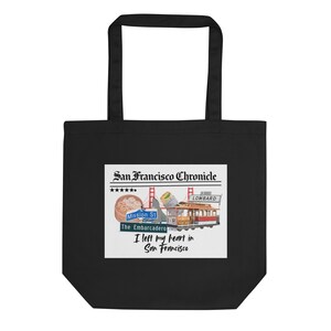 Pode incluir: Bolsa tote preta com um gráfico de São Francisco. O design inclui um teleférico, a Golden Gate Bridge e o texto "San Francisco Chronicle" e "I left my heart in San Francisco."