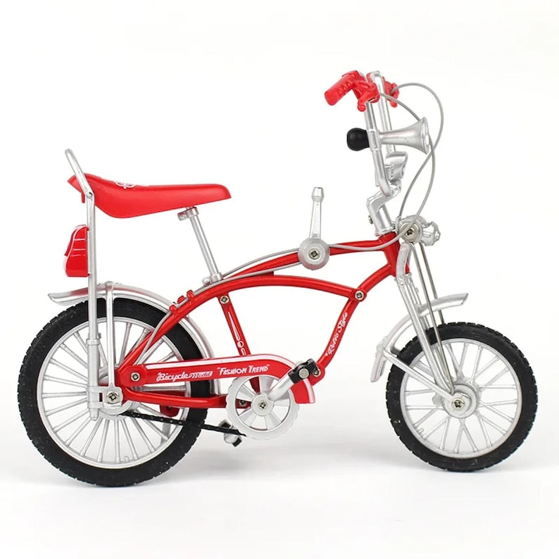May include: A miniature red bicycle with silver accents. The bike features a red seat, handlebars, and fenders. The tires are black, and the frame has the words "Bicycle" and "Fashion Trend" printed on it. A decorative item.