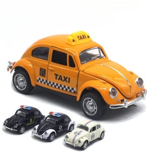Puede incluir: Un coche de juguete taxi de color naranja brillante con la palabra «TAXI» impresa en el lateral y un letrero amarillo en la parte superior. En primer plano hay tres coches de juguete más pequeños: dos coches de policía y un coche blanco con rayas de carreras y el número «53».