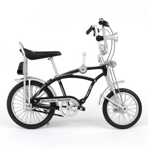 May include: A miniature black and silver bicycle with a high handlebar, horn, and a black seat. The bike has a classic design with the words "Bicycle Fashion Trend" on the frame. The tires are black.