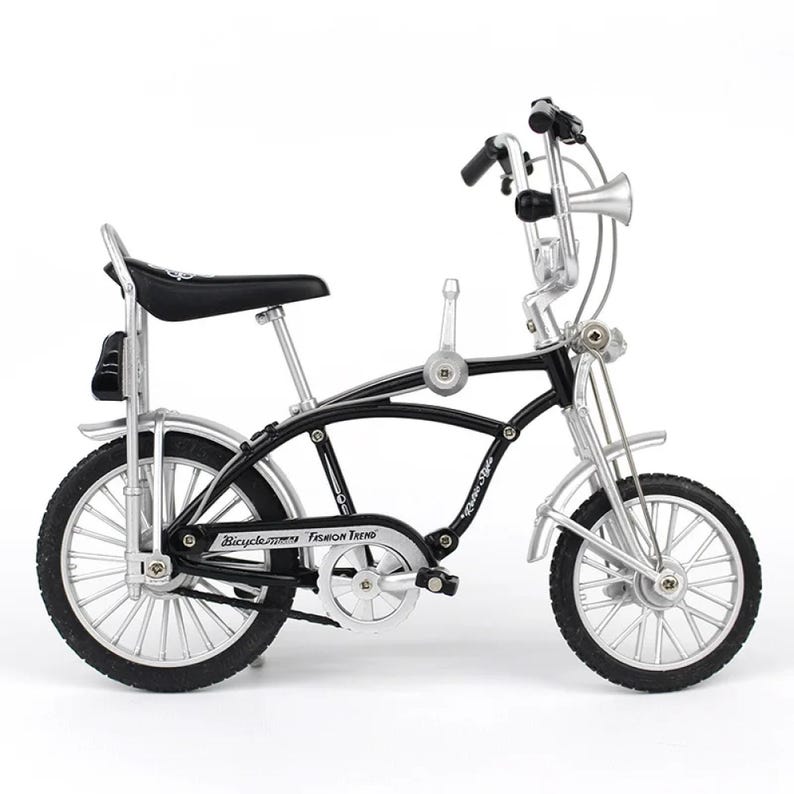 May include: A miniature black and silver bicycle with a high handlebar, horn, and a black seat. The bike has a classic design with the words "Bicycle Fashion Trend" on the frame. The tires are black.