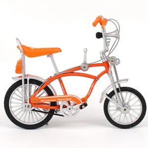 May include: An orange and silver retro-style bicycle with a high handlebar, horn, and a seat. The bicycle has black tires and the words "Bicycle Trend Fashion Trend" are printed on the frame.