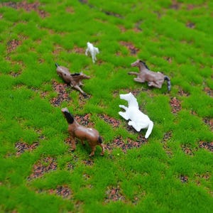 Puede incluir: Pequeños caballos de juguete en varias poses, incluyendo de pie y tumbados, dispersos sobre un lecho de césped artificial verde brillante. Los caballos son principalmente marrones y blancos, creando una escena juguetona.