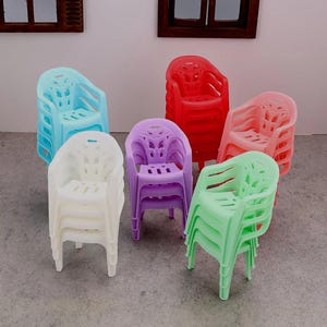 May include: A collection of miniature plastic chairs in various colors, including blue, white, red, pink, purple, and green. The chairs are stacked in groups, showcasing their design and form. The chairs have armrests and a slatted back.