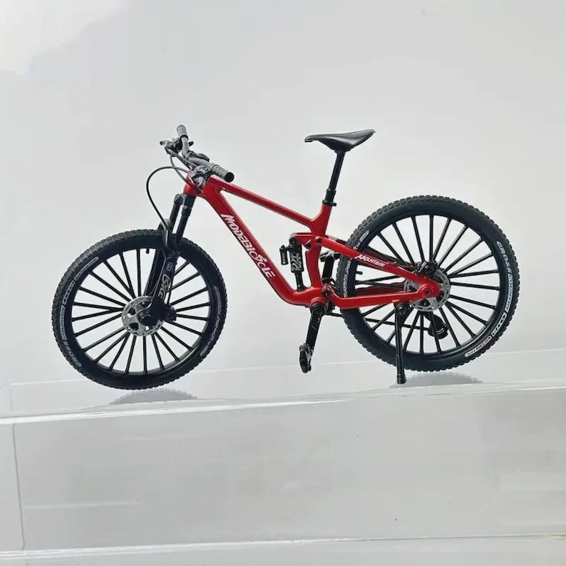 Op de afbeelding: Een rode mountainbike met zwarte banden en velgen. Op het frame van de fiets staat "MODEBIKE". De fiets heeft een zwart zadel en stuur. De banden hebben een noppenprofiel.