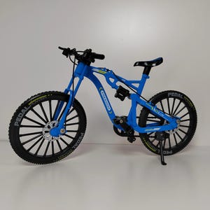 May include: A blue mountain bike model with black tires and rims. The bike has the word "FREEDOM" printed on the frame and "PEDAL POWER" on the tires. The bike is a miniature replica.