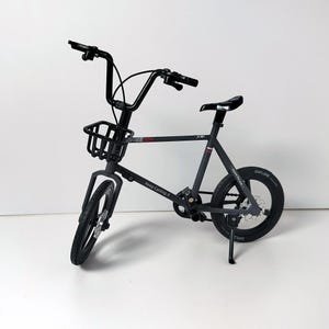 May include: A black miniature bicycle with a basket, handlebars, and a seat. The bike has the text "FREE.COM" on the frame and "Keep Cycling !" on the frame. The tires are black, and the bike is on a white surface.