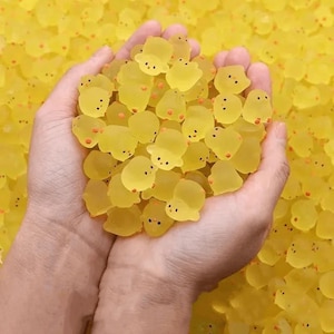 Può includere: Primo piano di una manciata di caramelle traslucide gialle a forma di pulcino, con occhi neri e becchi arancioni. Altre caramelle riempiono lo sfondo, creando una scena luminosa e allegra.