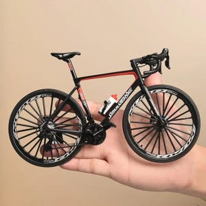 May include: A miniature black and red road bicycle with white accents. The bike features a water bottle, detailed wheels, and the text "Simulate Bike". The bicycle is a detailed model.