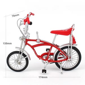 May include: A miniature red bicycle with silver accents. The bike features a red seat, handlebars, and frame. The dimensions are 6.85 inches long, 5.31 inches high, and 3.07 inches wide. The tires are black, and the bike has a classic design.