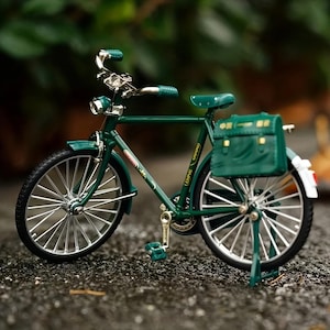 May include: A miniature dark green bicycle with silver detailing. The bike has a green saddle, handlebars, and a rear bag. The wheels have silver spokes and black tyres. A decorative item.