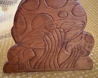 May include: A wooden coaster holder carved in the shape of mushrooms. The holder is brown with a detailed relief design of several mushrooms. The background is a light yellow fabric with a white polka dot pattern.