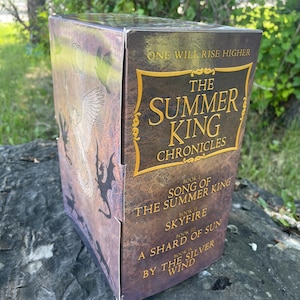 May include: A boxed set of "The Summer King Chronicles" books. The box is brown with gold lettering and features a fantasy-themed illustration. The titles of the books are "Song of the Summer King", "Skyfire", "A Shard of Sun", and "By the Silver Wind".