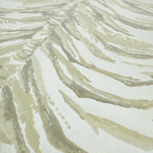 May include: Close-up of a fabric with a repeating pattern of abstract, curved lines. The lines are in shades of beige and gray, creating a textured, wave-like design against a white background. The fabric appears to be a woven material.