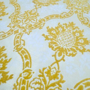 Może przedstawiać: Zbliżenie kremowej tkaniny z powtarzającym się wzorem żółtych kwiatów i wzorów zwojów. Wzór jest w klasycznym stylu damasceńskim, z żółtymi elementami lekko podniesionymi, tworząc efekt tekstury.
