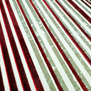 May include: Close-up of a fabric with a repeating pattern of diagonal stripes. The stripes alternate between deep red, light grey, and white. The red stripes have a textured appearance, while the grey stripes have a distressed look.