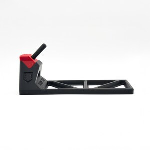 Pode incluir: Um suporte de pl&aacute;stico preto e vermelho com uma base horizontal com padr&atilde;o de recortes triangulares e um bra&ccedil;o de suporte vertical. A palavra PRNTO est&aacute; gravada na lateral da estrutura preta e um pequeno &iacute;cone de escudo sob a parte superior vermelha.