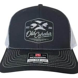 Può includere: Cappellino da camionista nero e bianco con visiera curva e retro in rete bianca. Il pannello frontale presenta una toppa con la scritta "Old Cahaba Hat & Apparel Co." e una grafica di uccelli. Il cappellino è regolabile.