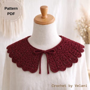 May include: A burgundy crochet collar with a scalloped edge and a small bow at the front. The collar is displayed on a mannequin and is paired with a white blouse. The text "Pattern PDF" is in the upper left corner.