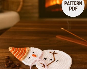 Könnte beinhalten: Handgefertigte Schneemann-Untersetzer aus Häkelarbeit. Der Schneemann hat einen weißen Körper, eine orange-weiß gestreifte Mütze und gestickte Details. Die Untersetzer liegen auf einer Holzoberfläche mit Kaffeebohnen. Der Text "PATTERN PDF" ist sichtbar.