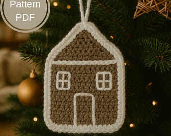 Puede incluir: Adorno navideño tejido a ganchillo con forma de casa. La casa es marrón con detalles blancos, incluyendo el tejado, la puerta y los marcos de las ventanas. El adorno está colgado de un árbol de Navidad. El texto "Pattern PDF" está en un círculo en la esquina superior izquierda.