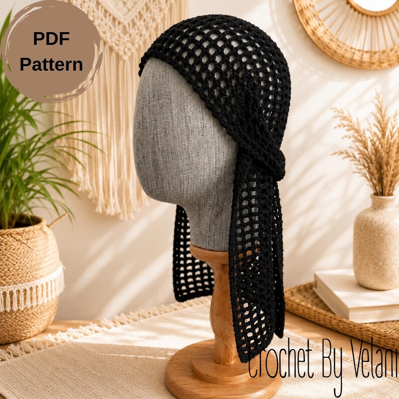 May include: A black crochet headscarf featuring an open mesh pattern with long ties on each side. The headscarf is displayed on a gray mannequin head stand. The image includes text that reads PDF Pattern and Crochet By Velani.