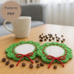 May include: Two handmade crochet coasters with a green scalloped edge and a white center, adorned with red stitching and a red bow. The coasters are displayed on a wooden table with coffee beans and a white mug. The image includes the text "Pattern PDF".