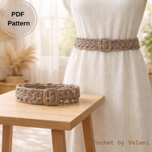 以下が含まれることがあります： 長方形のバックルが付いた、薄茶色の手編みのベルトが木製のテーブルに置かれています。ベルトには花柄があります。2つ目のベルトは白いドレスに巻かれています。「PDF Pattern」の文字が左上に円で表示されています。