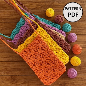 Puede incluir: Una colección de bolsos de ganchillo hechos a mano en colores vibrantes: naranja, amarillo, turquesa, morado y marrón. Cada bolso tiene una correa y se muestra sobre una superficie de madera. Varias madejas de hilo en colores a juego están dispersas alrededor de los bolsos. La imagen incluye un gráfico "PATTERN PDF".