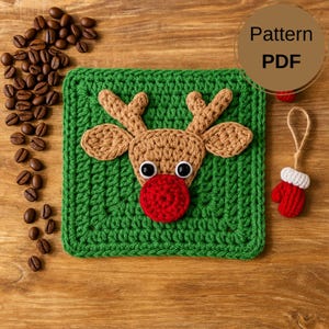 Op de afbeelding: Een groen gehaakt vierkant met een rendiergezicht, met een bruine kop en geweien, een rode neus en zwarte ogen. Een klein rood en wit gehaakt wantenornament hangt in de buurt. De afbeelding bevat ook koffiebonen en de tekst "Pattern PDF".