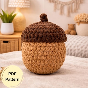 May include: A handmade acorn-shaped storage basket in shades of brown and tan. The top is a darker brown, and the body is a lighter tan color. The text "PDF Pattern" is in a yellow circle.