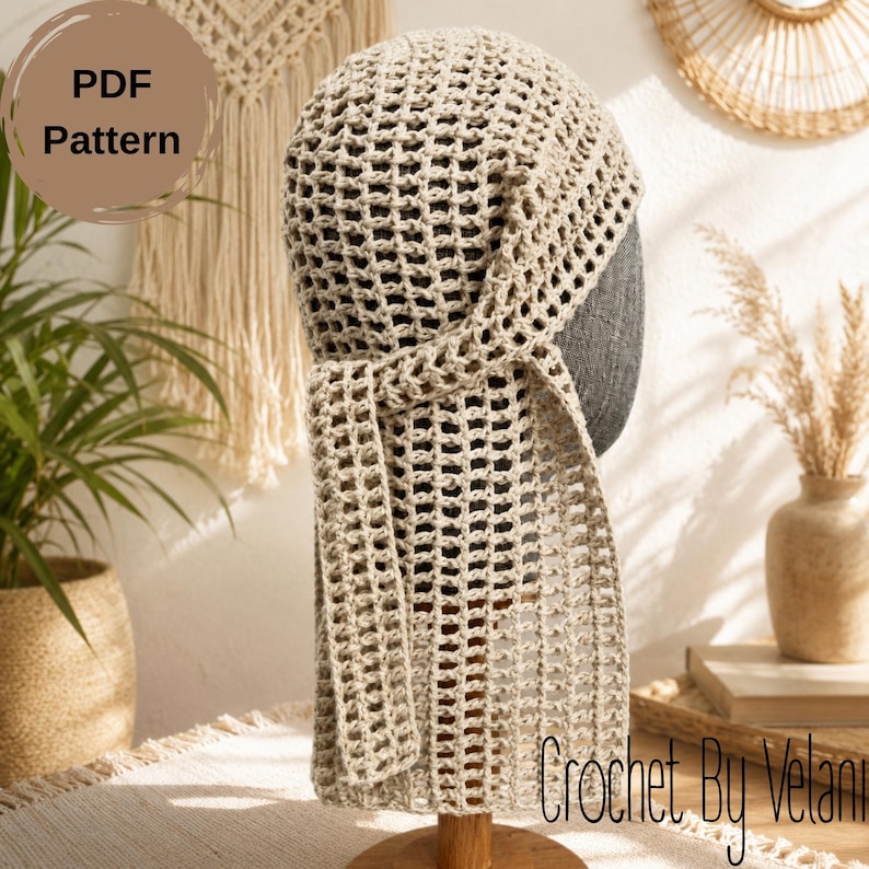 May include: A beige crochet head covering featuring an open grid pattern and a long, dangling side tie. The item is displayed on a dark gray mannequin head. A circular brown graphic in the upper left corner contains the text PDF Pattern.
