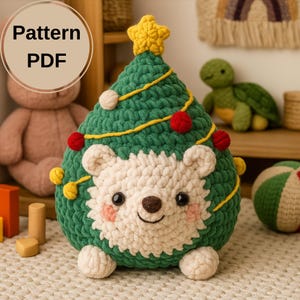 Op de afbeelding: Een groen en witte gehaakte kerstboom met een lachend berengezicht. De boom is versierd met rode en witte ornamenten, een gele ster en gele lichtslingers. De tekst "Pattern PDF" staat in een cirkel linksboven.
