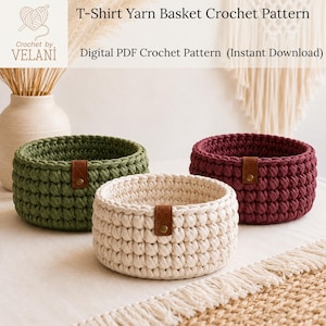 May include: Three round crochet baskets made from thick t-shirt yarn in olive green, cream, and burgundy. Each basket features a small brown faux leather tag attached with a gold-colored metal rivet. The text reads T-Shirt Yarn Basket Crochet Pattern.