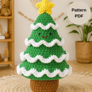 Puede incluir: Un árbol de Navidad de ganchillo verde hecho a mano con adornos blancos y una estrella amarilla en la parte superior. El árbol tiene una cara sonriente y está en una maceta marrón. La imagen incluye el texto "Pattern PDF".