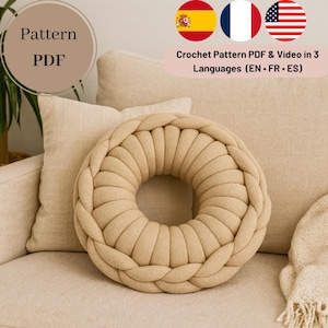 May include: A beige, donut-shaped crochet pillow with a braided edge sits on a beige sofa. The image includes text that says "Pattern PDF" and "Crochet Pattern PDF & Video in 3 Languages (EN • FR • ES)".