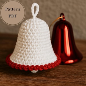 Op de afbeelding: Een witte gehaakte bel met een rode rand, naast een glanzende rode belornament. De afbeelding bevat de tekst "Pattern PDF". De bel heeft een lus om op te hangen.