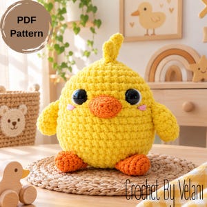May include: A yellow crochet chick plush toy with a round body, orange beak, and orange feet. The chick has large black safety eyes and small pink stitched cheeks. A circular badge in the top left corner reads PDF Pattern, and text in the bottom right reads Crochet By Velani.