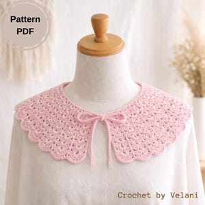May include: A light pink, crocheted collar with a scalloped edge and a delicate bow at the front. The collar is displayed on a mannequin and is part of a PDF pattern. The text "Crochet by Velani" is visible.