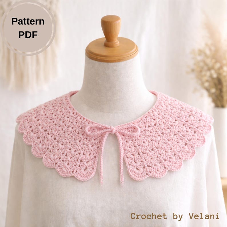 May include: A light pink, crocheted collar with a scalloped edge and a delicate bow at the front. The collar is displayed on a mannequin and is part of a PDF pattern. The text "Crochet by Velani" is visible.
